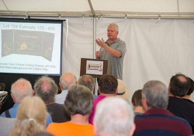 Auctioneer in front of audience, inside event tent.